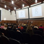 Full room shot of Peter Weishar and Lisa Waxman introducing the keynote speaker