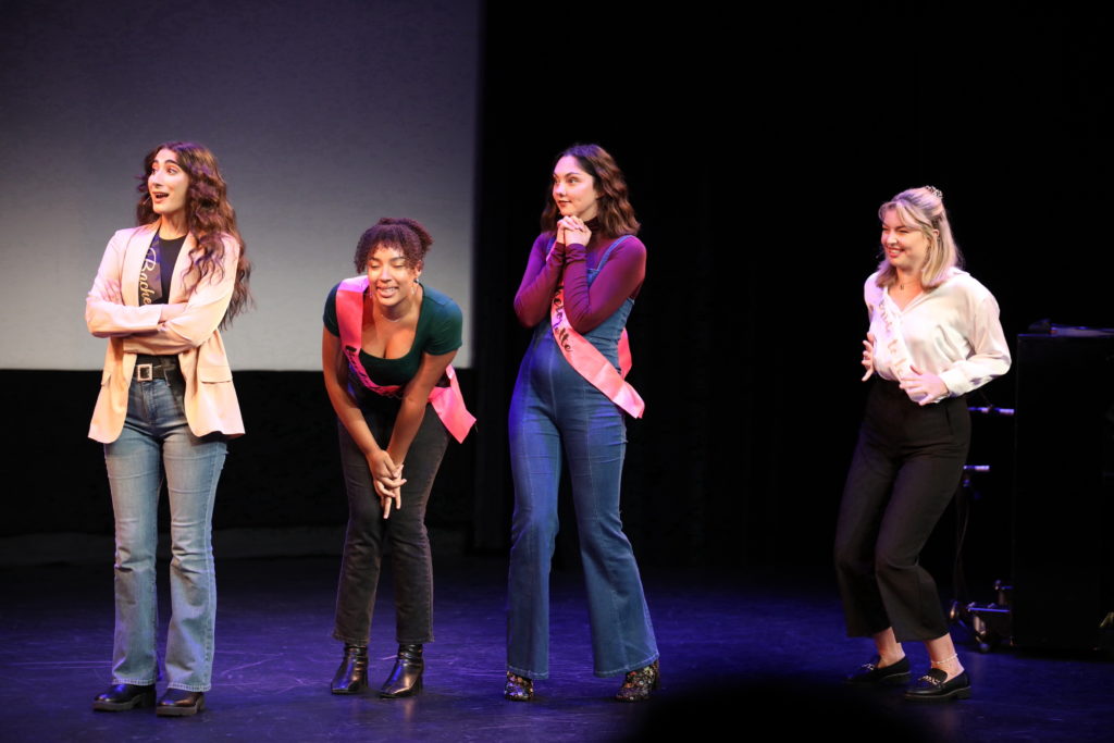 Four women stand on stage looking excited.