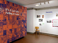 An orange and purple wall features book covers from Naiad Press. To the right, ephimera from the press hangs on the wall of the MoFA.