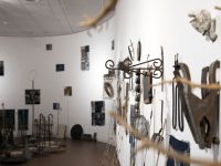 An art installation hangs on a white gallery wall. It is made up of a wide variety of seemingly found objects juxtaposed with