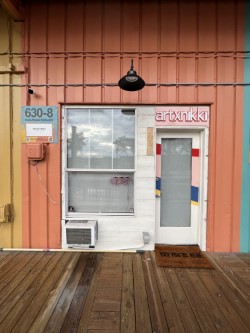 A brightly colored small building with a neon sign that reads "artxnikki"