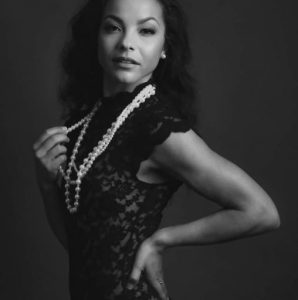 Richardson poses in a black dress, wearing a pearl necklace.