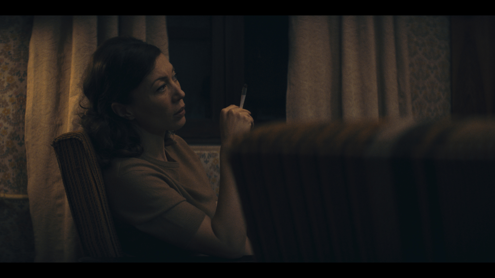 A woman in a darkly lit room smoking a cigarette. 