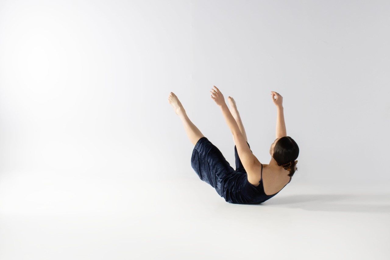 A dancer is on her back, with her arms and legs outstretched, her body curving. 
