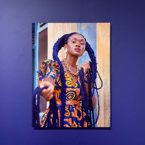 A photograph of a woman in an African print dress displayed on a blue wall. 