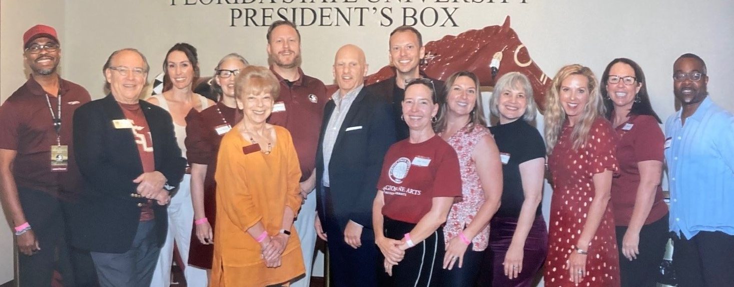 A group of smiling people in garnet and gold post in the University President's Box in this keepsake photo. 