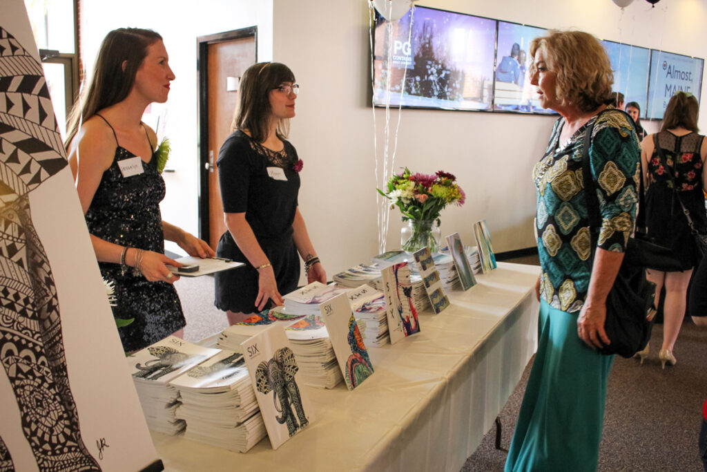 Young people standing at a table showing magazines to others,