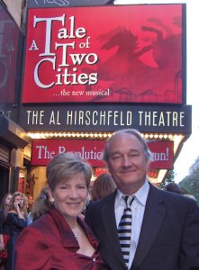 A man and woman dressed for a special occasion pose in front of a broadway sign, which reads "A Tale of Two Cities."