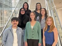 A group of smiling graduate students pose on a staircase