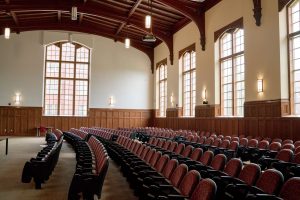 A beautiful auditorium with red seats, lit by tall windows