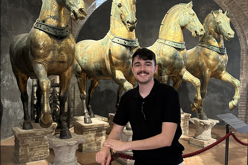 a young man poses for a photo in front of statues of horses