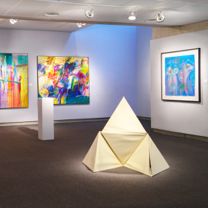 there is a sculpture of a pyramid in the middle of a room with paintings on the walls