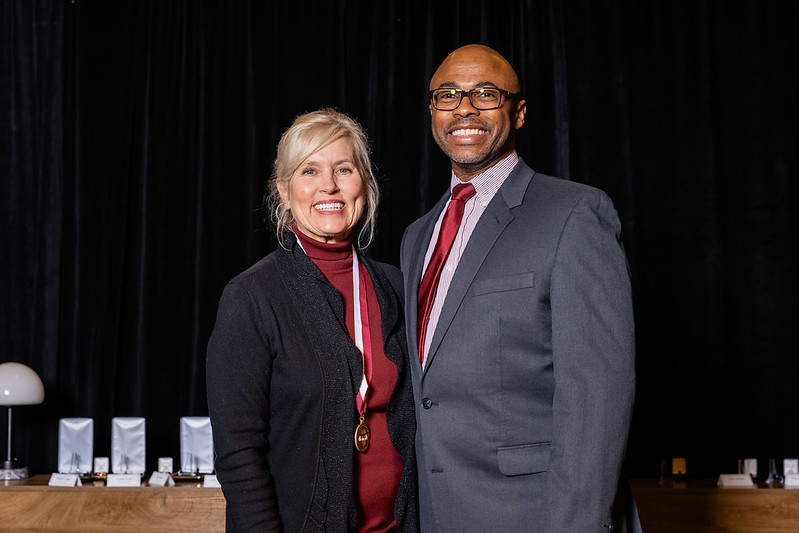 A man and woman pose for a photo in professional attire at an awards ceremony. 
