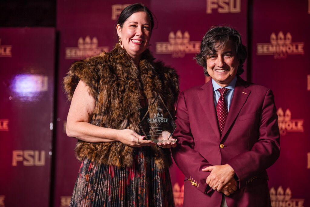 A man and woman pose in front of a garnet and gold FSU backdrop