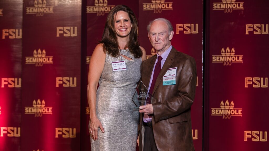 A man and woman pose in front of a garnet and gold FSU backdrop