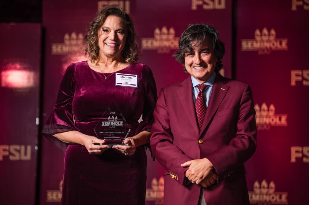 A man and woman pose in front of a garnet and gold FSU backdrop