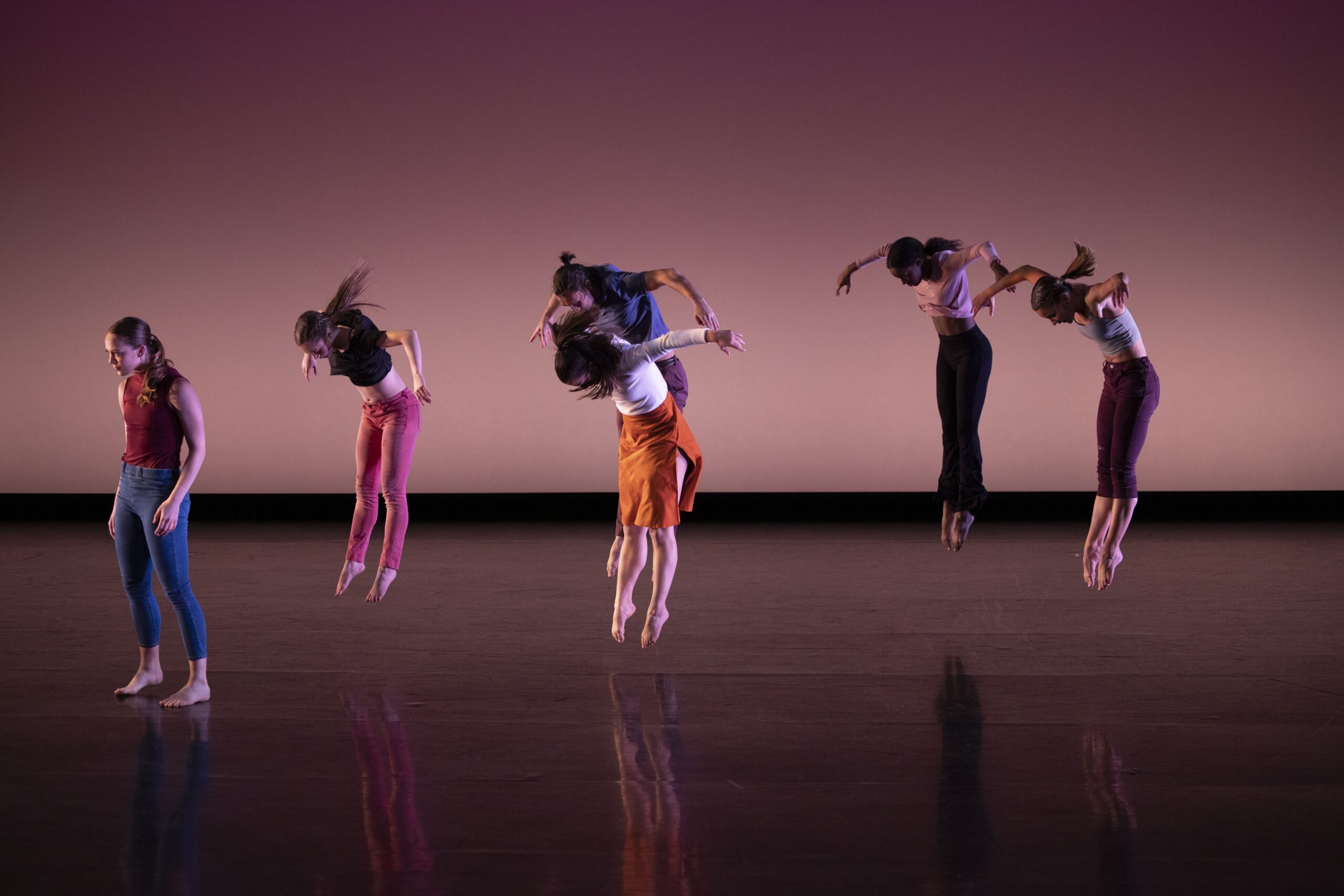 six people jumps except one on stage in coordination for a dance