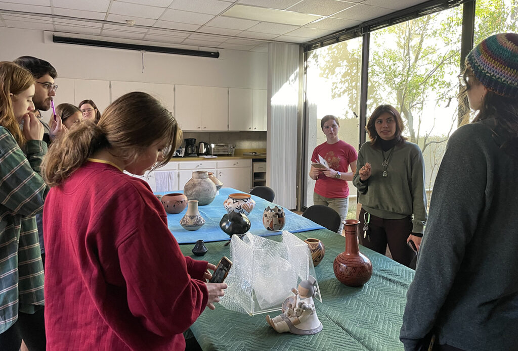 A group of people stand around a table, looking at indigenous artifacts.