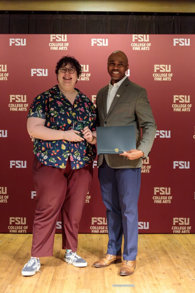 Two people pose in front of a backdrop, garnet with FSU Fine Arts logos scattered about.