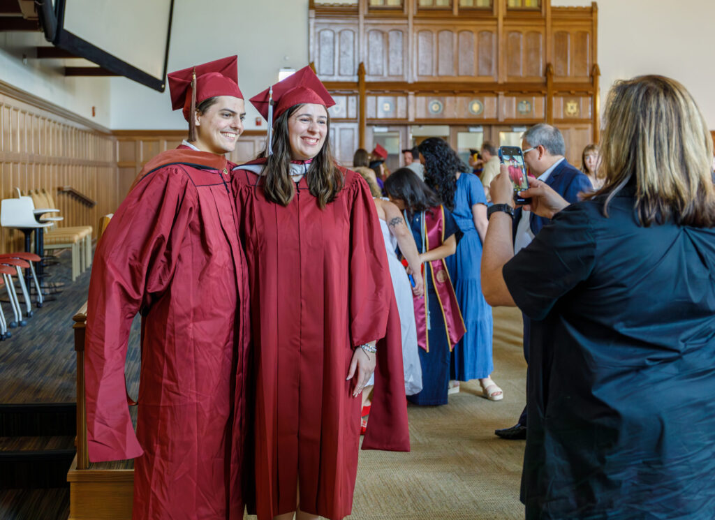 Two graduates smiling and posing for a picture in garnet caps and gowns