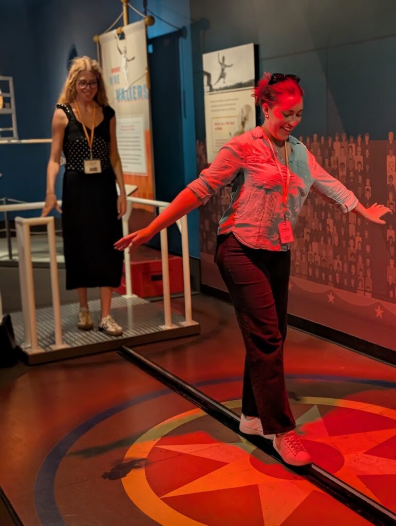 A woman in a museum walks on a model tight rope as part of an interactive exhibit. 