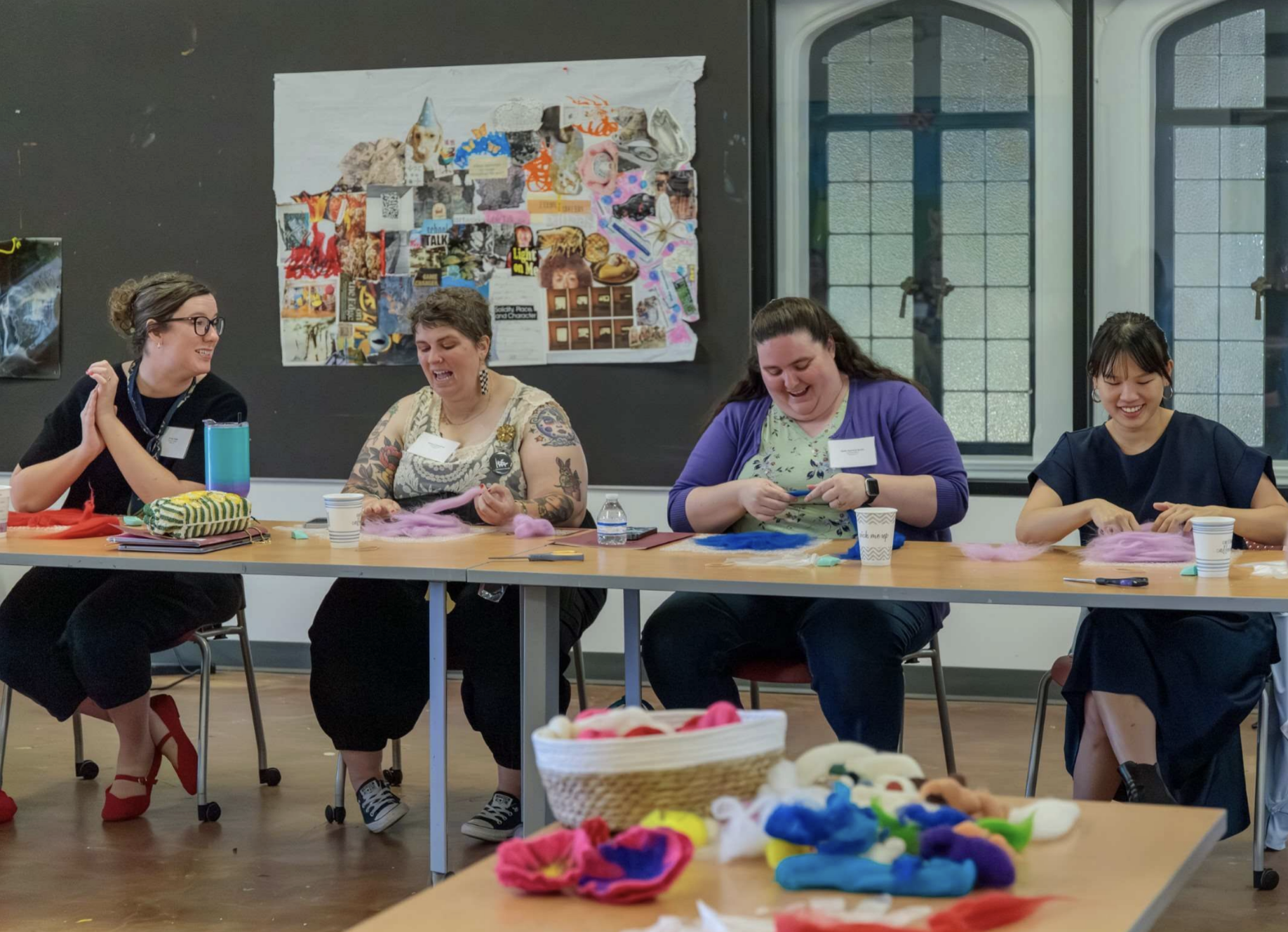 Adult women seated at a table making art and laughing.