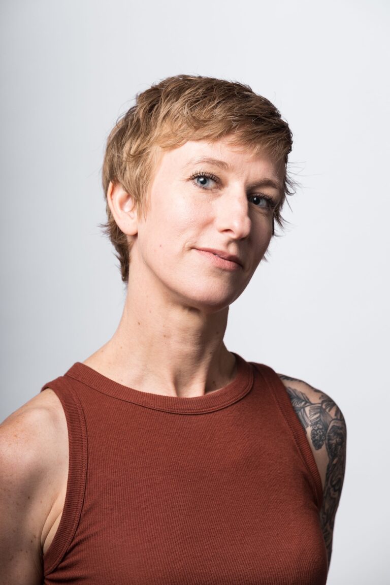 A woman with short blonde hair in a rust colored tank top.