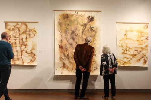 A man and woman admire a large earthtone piece of art in a gallery