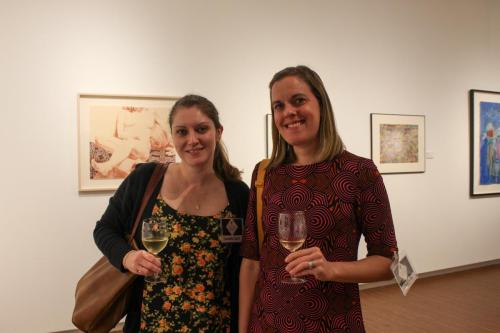 Two women holding wine glasses smile for a photo in an art gallery