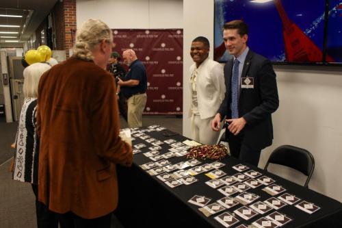 Two young people stand to meet event guests at a table covered in name tags.
