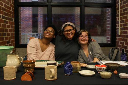 Three young people pose behind a table full of pottery